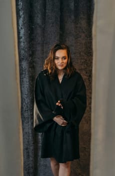 A woman standing in front of a curtain, with neutral expression and hands by her sides. Vertical frame.