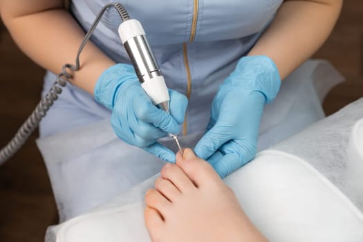 Young woman getting professional pedicure with milling cutter in beauty salon.