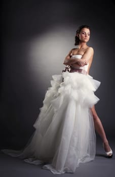 Graceful brunette posing covered by wedding dress, on gray background