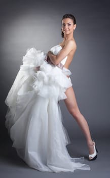 Smiling naked model covered by wedding dress, on gray background