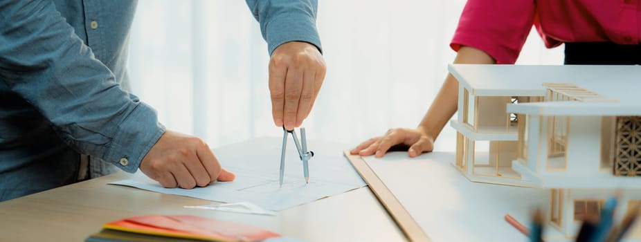 Professional architect team select sustainable house materials while skilled engineer using divider measure blueprint with house model and color palette placed on meeting table. Closeup. Variegated.