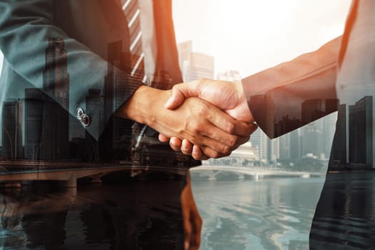 Double exposure image of business people handshake on city office building in background showing partnership success of business deal. Concept of corporate teamwork, trust partner and work agreement.