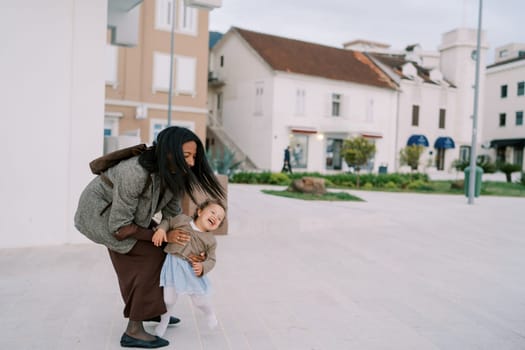 Smiling mother catches laughing little girl running near house. High quality photo