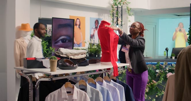 Meticulous worker changing clothes on mannequin after restocking elegant high end fashion boutique. Precise employee changing old season clothing with stylish garments from new collection