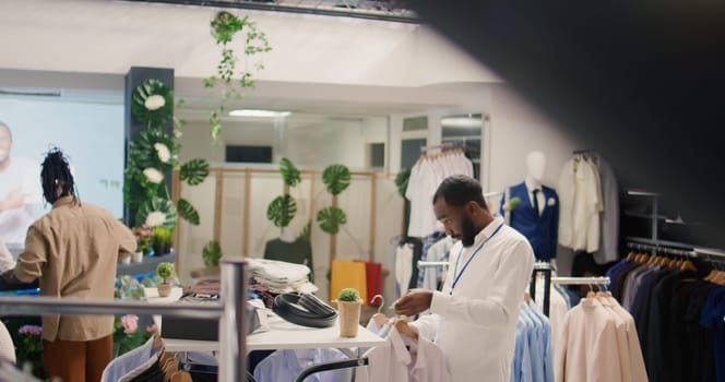 Overhead shot of employee arranging formalwear clothes on racks in clothing store, sorting every item by fit size. Retail assistant arranging garments in expensive fashion boutique