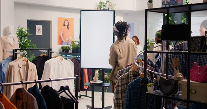 Customer in shopping outlet using AR tech kiosk to look at cheap and sustainable clothes. Client in eco friendly second hand store using led screen to choose between garments
