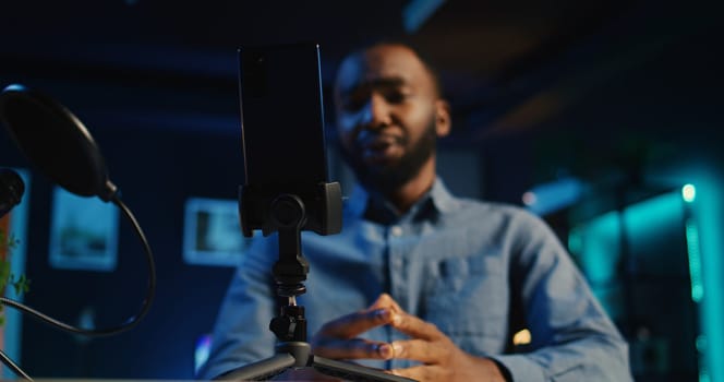 Close up of cellphone on holder and microphone used by online star in dimly lit home studio to film video for online platforms. Phone being used by african american influencer to record footage