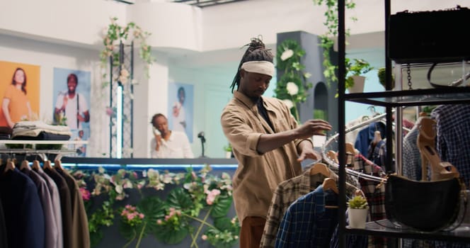 Tracking shot of customer in clothing store during promotional season looking to purchase cheap garments. Client taking advantage of sales in fashion boutique, looking at clothes on racks