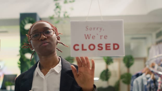African american shop assistant closing fashion boutique business, ending her shift at night. Storekeeper turning opened sign on fast fashion clothing store into closed one after working hours