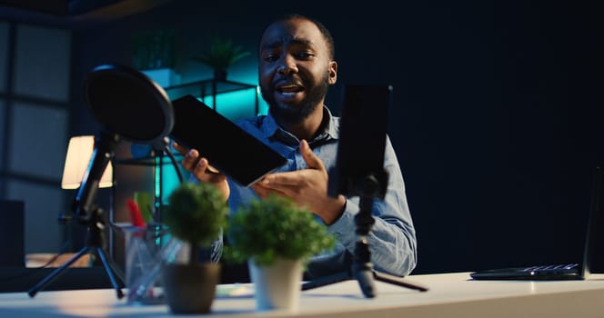 Content creator in studio films tablet video review for tech enthusiasts. African american viral online star hosts technology internet show, unboxing digital portable device