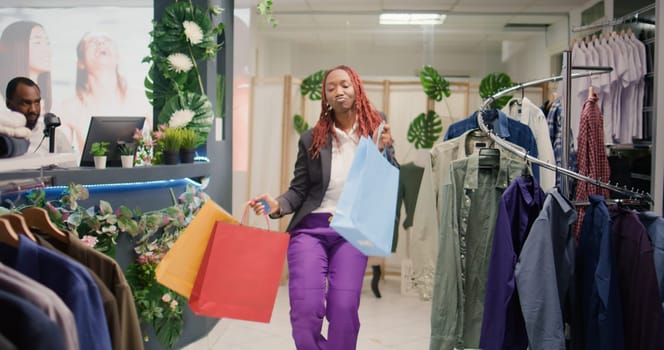 Customer excited after finding cheap and sustainable designer clothing in zero waste shopping outlet. Woman dancing with shopping bags in hand in eco friendly second hand store