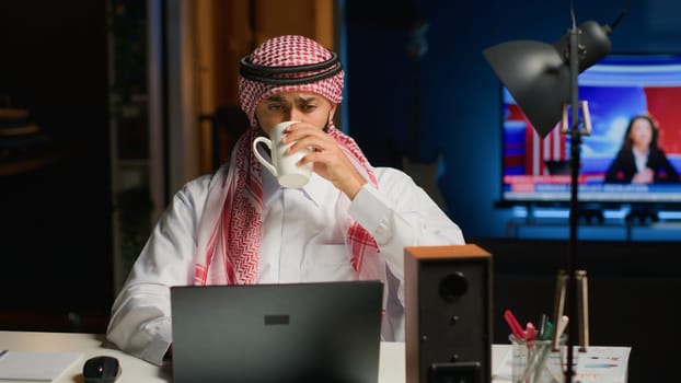 Arab job candidate enjoying beverage while remotely being interviewed by human resources team. Muslim man drinks coffee while getting his credentials checked during online video conference meeting