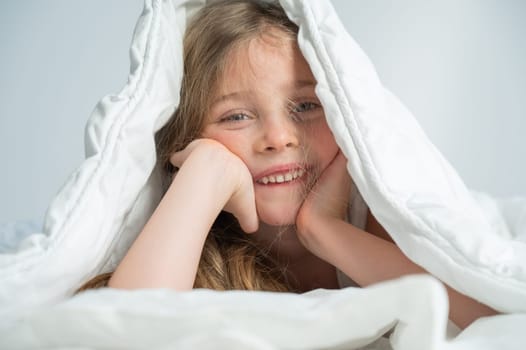 Portrait of a cute little girl laughing and hiding under the blanket