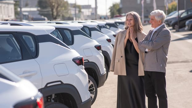 Mature Caucasian couple walks past cars outdoors, choosing a new one