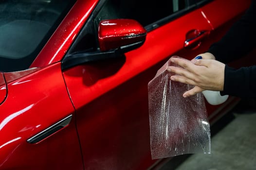 A technician sprays water before applying protective vinyl film to a car