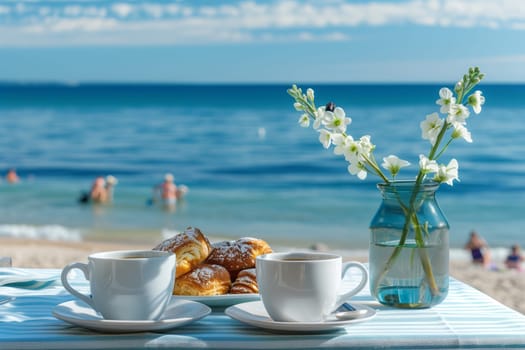 Two cups of coffee and croissants arranged on a table with azure sky and fluffy clouds in the background, surrounded by blooming flowers on the beach