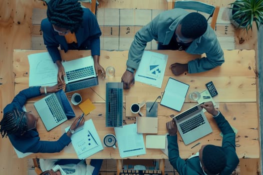 A group of individuals are gathered around a wooden table with laptops, sharing information on personal computers. The laptops serve as output devices in this office setting