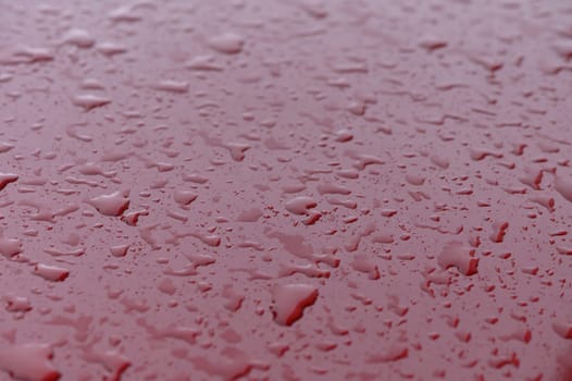 Hydrophobic water effect on red car paint after rain. Water drops on metal surface