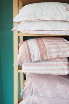 Pillows stacked on wood shelf in bedroom with linens,