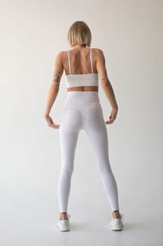 Beautiful blonde girl posing on a white background in white leggings and a white top. High quality photo
