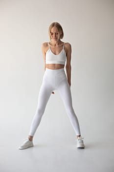 Beautiful blonde girl posing on a white background in white leggings and a white top. High quality photo