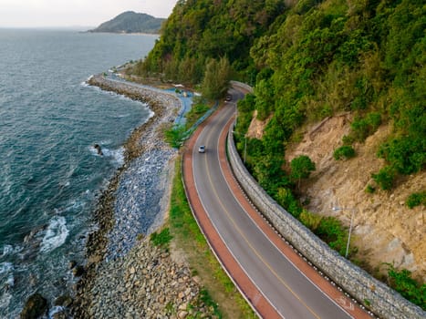 car driving on the curved road alongside the ocean beach road of Thailand. road landscape in summer. it's nice to drive on the beachside highway. Chantaburi Province Thailand, at sunset, drone view