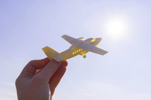 close up photo of male hand holding toy airplane against blue sky . image is retro filtered