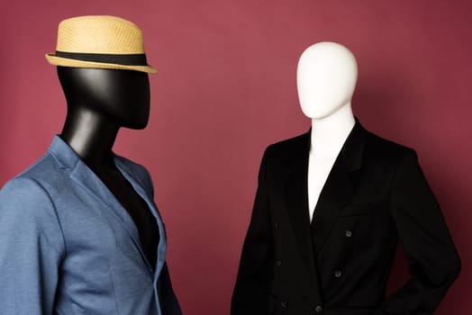 Two male mannequin in a black business suit and in a blue suit and white pants on a ruby background - image