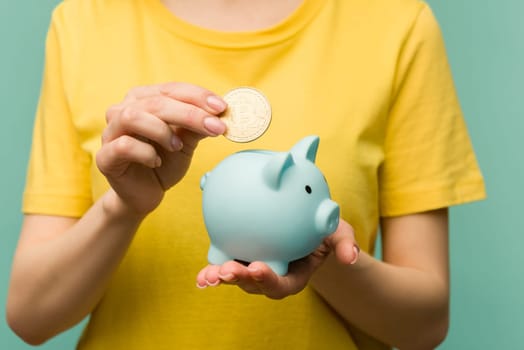 Female putting physical bitcoin into piggy bank, investment in cryptocurrency concept.