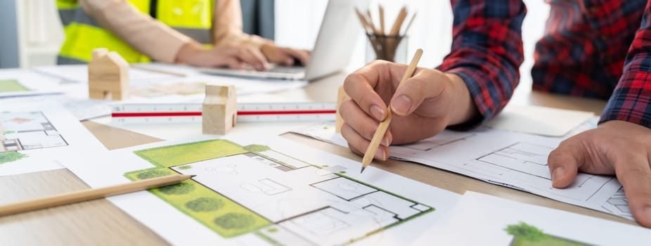 A cropped portrait of professional architect working with blueprint during safety engineer using laptop analysis data at meeting table with document scatter around. Close up. Delineation.