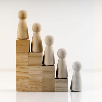 Wooden figures stand on the cubes that represent the stairs. The concept of social inequality or career growth.