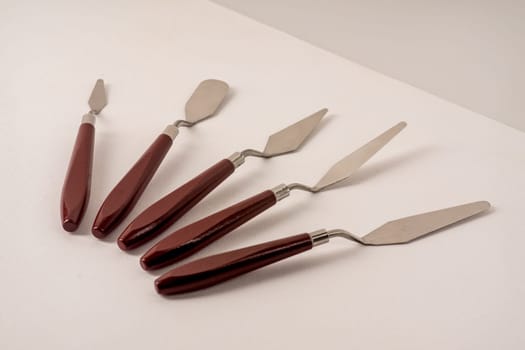 Five art palette knives lie on a white art canvas.