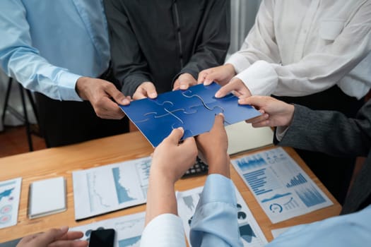 Corporate officer worker collaborate in office, connecting puzzle pieces with report paper on table as partnership and teamwork. Unity and synergy in business concept by merging jigsaw puzzle. Concord