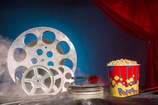 Old film reels, popcorn and 3d glasses on the table. Focus on glasses. Multicolored background. Evolution Film Media