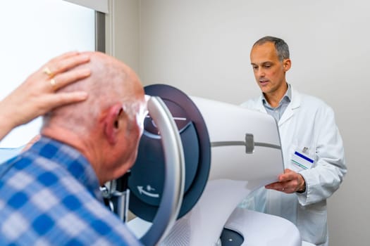 Rear view of a senior receiving a laser treatment for glaucoma in the eye in a clinic