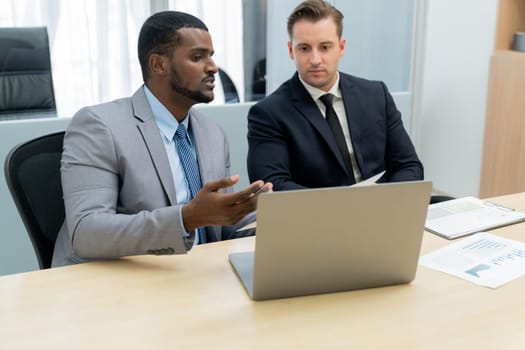 African male leader explain strategy while show solution to professional project manager by pointing at document, using laptop. Skilled business team brainstorming idea. Business meeting. Ornamented.