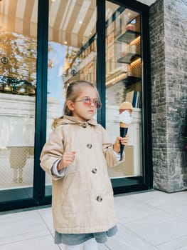 Little girl with a big ice cream cone stands near the glass door of the shop. High quality photo