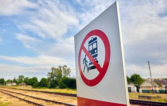 A concrete railway track under a sunny sky with a vivid prohibition sign displaying a train and a person, emphasizing no crossing. The scene captures rail safety on a lovely day.