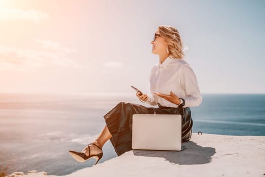 Digital nomad, Business woman working on laptop by the sea. Pretty lady typing on computer by the sea at sunset, makes a business transaction online from a distance. Freelance remote work on vacation