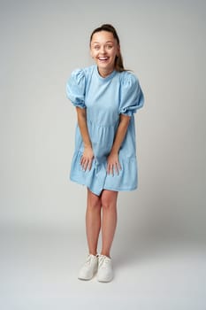 Young happy smiling woman in a light blue dress on a gray background close up