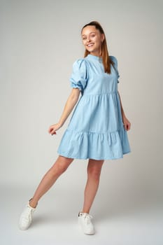 Young happy smiling woman in a light blue dress on a gray background close up