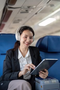 Asian young woman wearing headphone listen to music at first class on airplane during flight, Traveling and Business concept.