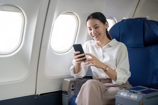 Traveling and technology. Flying at first class. Young business woman passenger using smartphone while sitting in airplane flight.