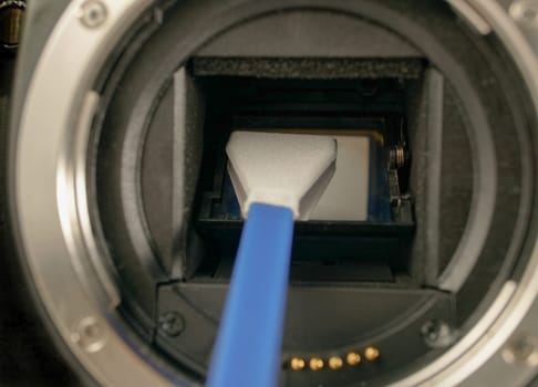 Technician cleans sensor of digital camera from dust and dirt using cleansing swab.
