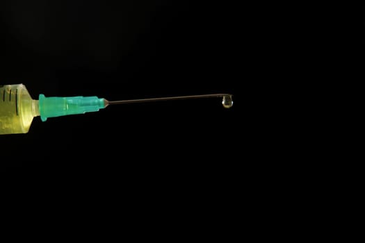 syringe with needle with a drop of liquid coming out, isolated on black background and copy space