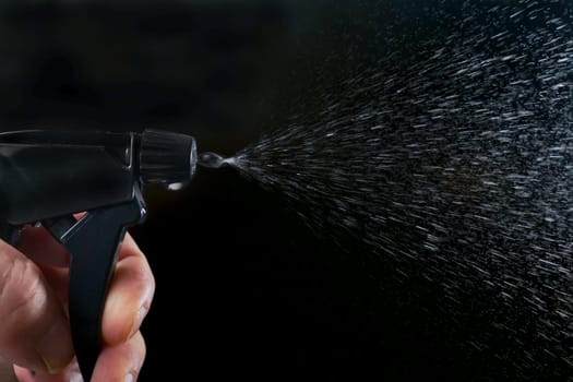 a man's hand pressing the trigger of a sprayer, spraying water droplets on a black background