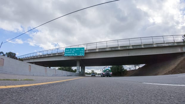 On a cloudy winter day, a car smoothly travels along Highway 101 near Santa Maria, California, under a cloudy sky, surrounded by a blend of greenery and golden hues.