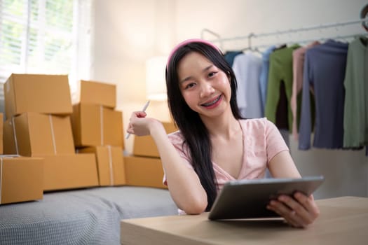 Young woman working online ecommerce shopping at her shop. Young woman sell prepare parcel box of product for deliver to customer. Online selling, ecommerce. Selling products online.
