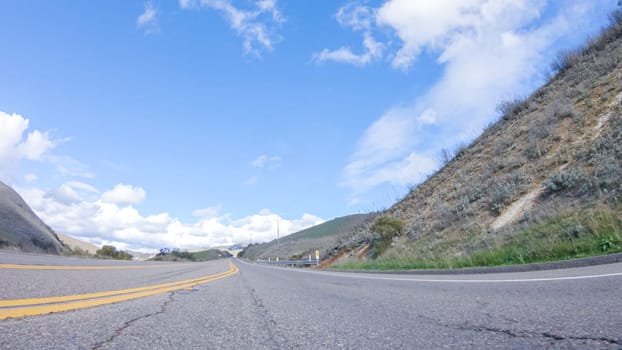 Vehicle is cruising along the Cuyama Highway under the bright sun. The surrounding landscape is illuminated by the radiant sunshine, creating a picturesque and inviting scene as the car travels through this captivating area.