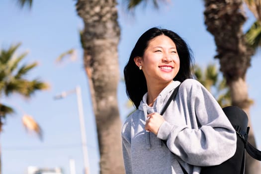 portrait of a young asian woman dressed in sportswear smiling happy while walking with yoga mat hanging on her arm, sport and healthy lifestyle concept